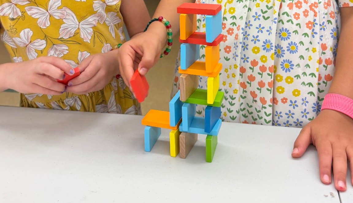 Two children stacking wooden blocks into a tall tower as a team