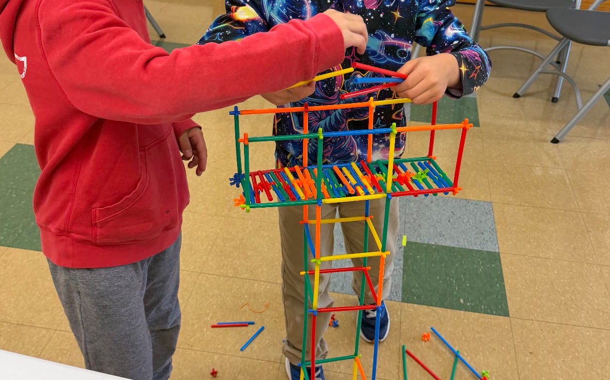Two kids working together to build a tall tower during the Building Bridges module