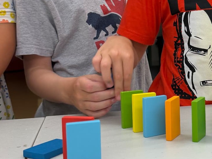 Two children working together to set up a line of colorful dominoes